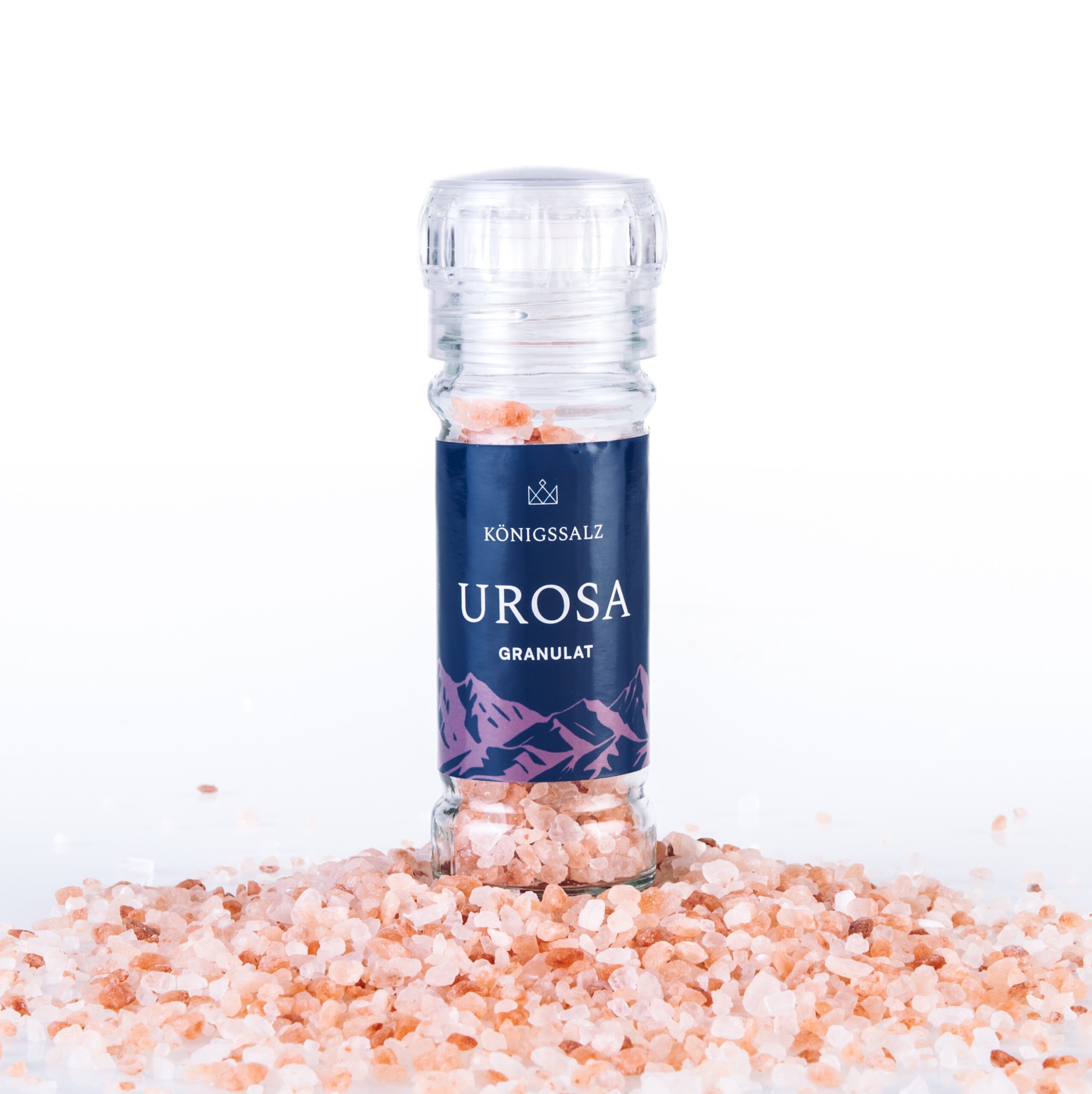 Königssalz Urosa: Rosa Himalayasalz Granulat in einer 100g Gewürzmühle. Nahaufnahme mit Mühle auf losen rosafarbenen Salzkristallen vor weißem Hintergrund